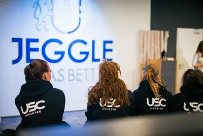 Vier Frauen im USC Münster Trainingsanzug sitzen vor einer Werbewand von Jeggle Betten.