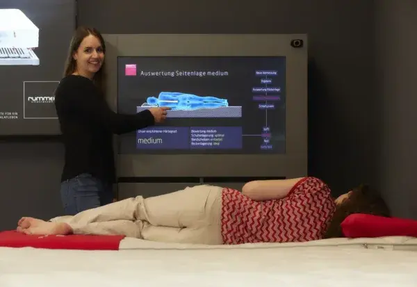 Eine Frau demonstriert eine digitale Liegeanalyse zur ergonomischen Matratzenberatung.