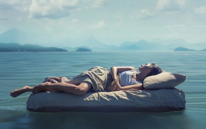 Frau entspannt auf einer Matratze auf ruhigem Wasser mit Bergen im Hintergrund bei Sonnenschein.