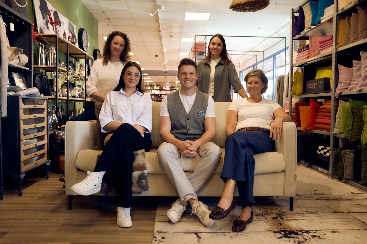 Fünfköpfiges Team sitzt auf Sofa im modernen Einrichtungsgeschäft mit Wohnaccessoires.